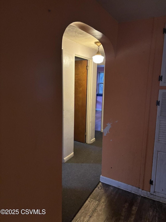 corridor featuring baseboards, arched walkways, and wood finished floors