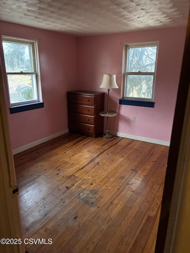 unfurnished bedroom featuring baseboards, multiple windows, a textured ceiling, and hardwood / wood-style floors