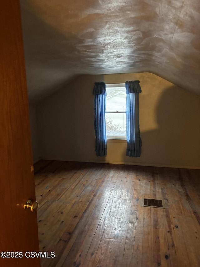 additional living space with visible vents, vaulted ceiling, and hardwood / wood-style flooring