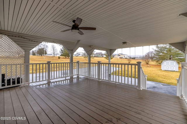 wooden terrace featuring a ceiling fan, an outbuilding, a lawn, and a storage shed