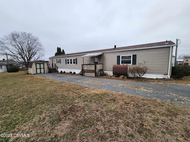 view of front of property with an outbuilding, a front yard, a shed, heating fuel, and aphalt driveway