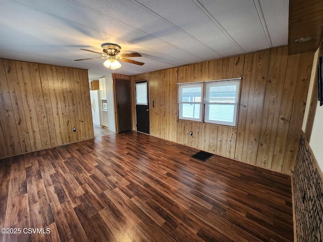 unfurnished room with wooden walls, visible vents, ceiling fan, and wood finished floors