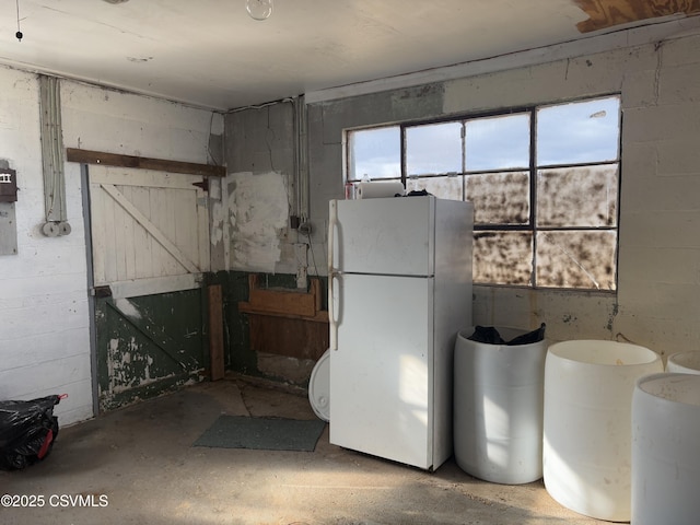 interior space featuring concrete block wall and freestanding refrigerator