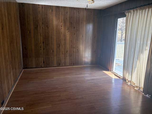 empty room featuring wood finished floors, wood walls, and a textured ceiling