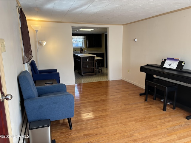 sitting room with light wood-type flooring, baseboards, and ornamental molding