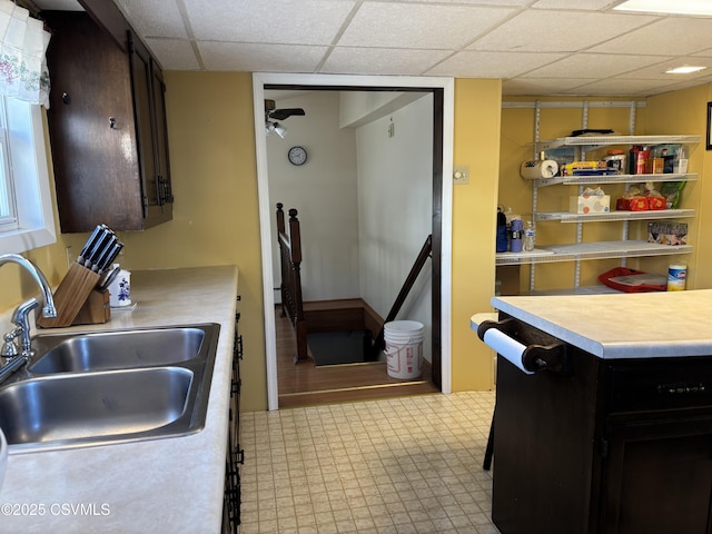 kitchen featuring light floors, ceiling fan, a sink, light countertops, and a paneled ceiling