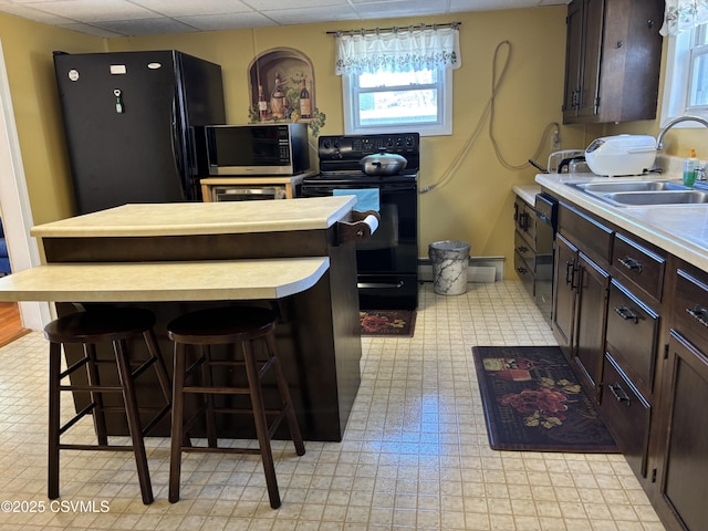 kitchen with a center island, dark brown cabinetry, a breakfast bar area, black appliances, and a sink