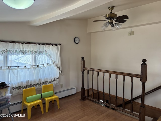 living area with a baseboard heating unit, wood finished floors, an upstairs landing, and ceiling fan