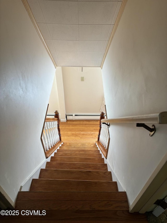 staircase featuring baseboard heating, wood finished floors, and crown molding