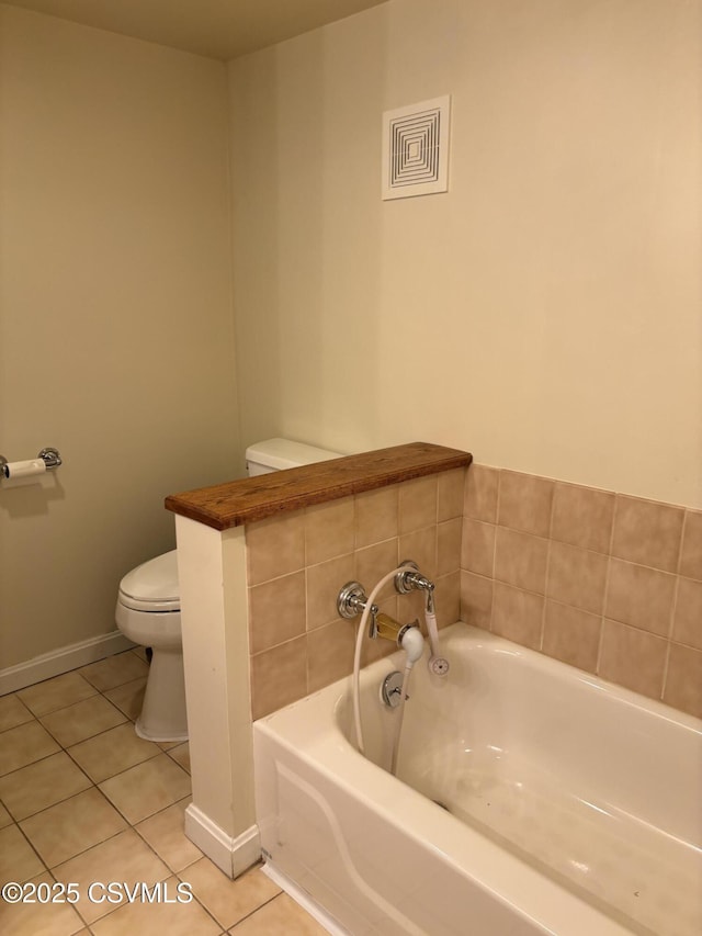 bathroom featuring tile patterned floors, baseboards, toilet, and a bath