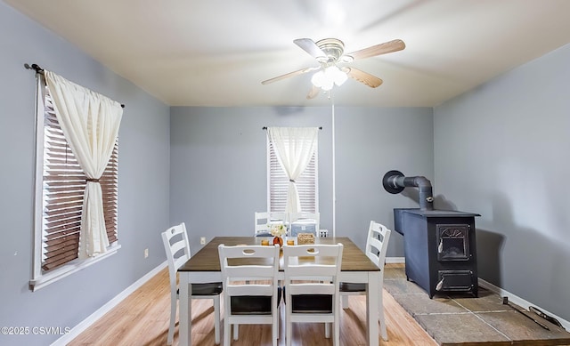 dining area with wood finished floors, a wood stove, a ceiling fan, and baseboards