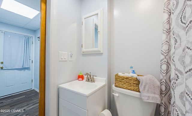 bathroom with a paneled ceiling, toilet, wood finished floors, and vanity