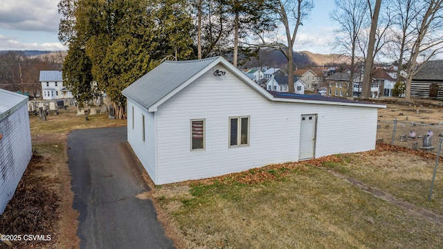 view of side of home featuring aphalt driveway, a yard, fence, and metal roof