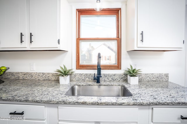 kitchen with white cabinetry, light stone countertops, and a sink