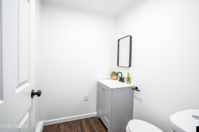 half bathroom featuring vanity, wood finished floors, baseboards, ornamental molding, and toilet