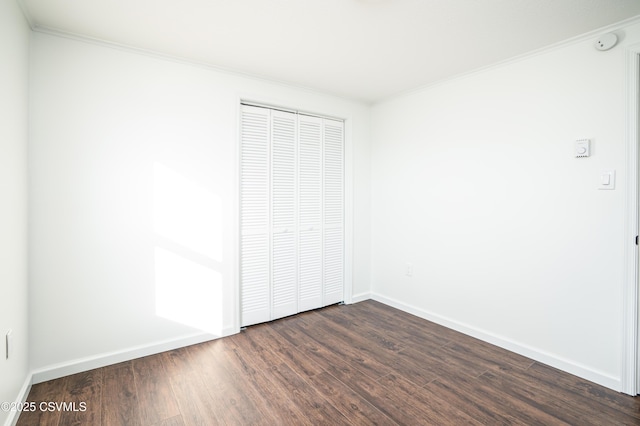 unfurnished bedroom featuring a closet, baseboards, dark wood-style flooring, and crown molding