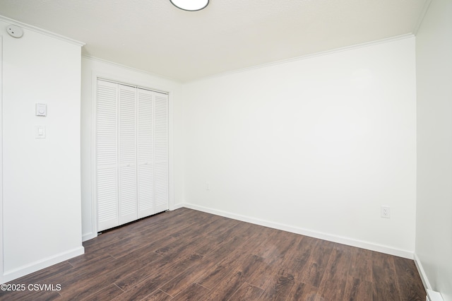 unfurnished bedroom featuring a closet, dark wood-style flooring, baseboards, and ornamental molding