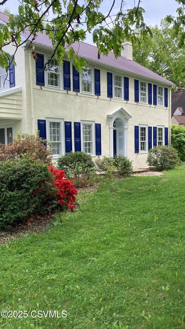 colonial house with stucco siding, a chimney, and a front yard