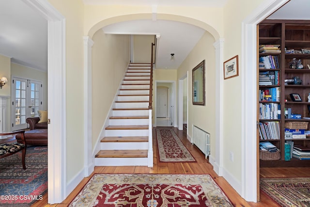 stairway with radiator heating unit, wood finished floors, arched walkways, and baseboards