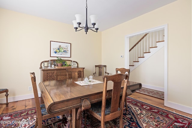 dining room featuring stairway, wood finished floors, baseboards, and a chandelier