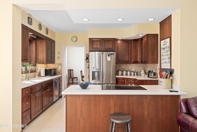 kitchen featuring a sink, stainless steel appliances, a peninsula, light countertops, and decorative backsplash