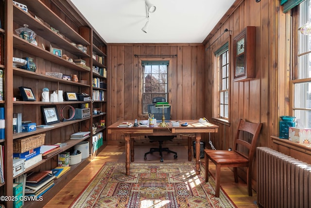 home office with track lighting, radiator, wood finished floors, and wooden walls