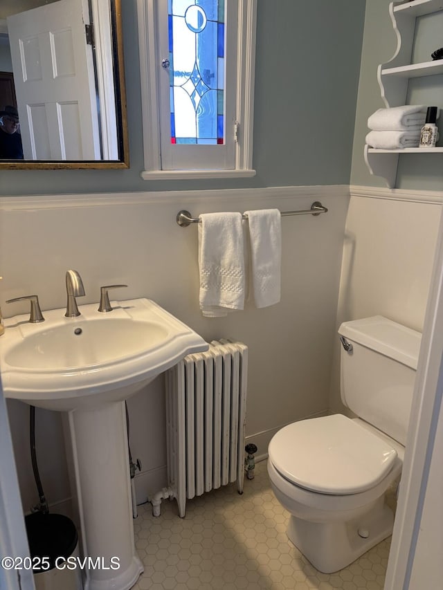 half bathroom featuring tile patterned floors, radiator, toilet, and a sink