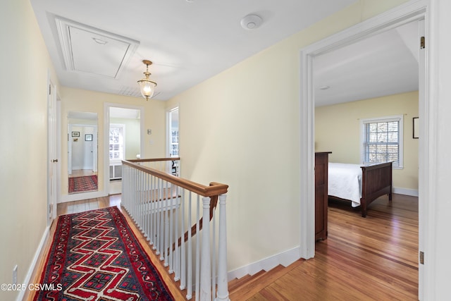 corridor with an upstairs landing, attic access, baseboards, and wood finished floors