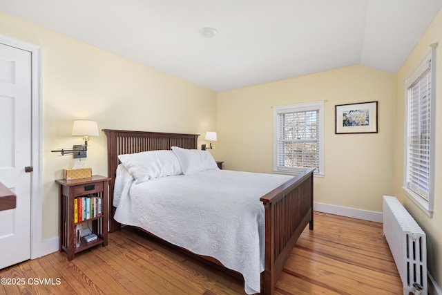 bedroom with baseboards, lofted ceiling, wood finished floors, and radiator heating unit