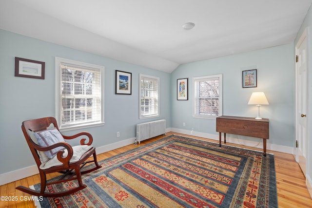 living area featuring vaulted ceiling, radiator, wood finished floors, and baseboards