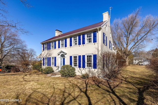 colonial house featuring stucco siding, a front lawn, and a chimney