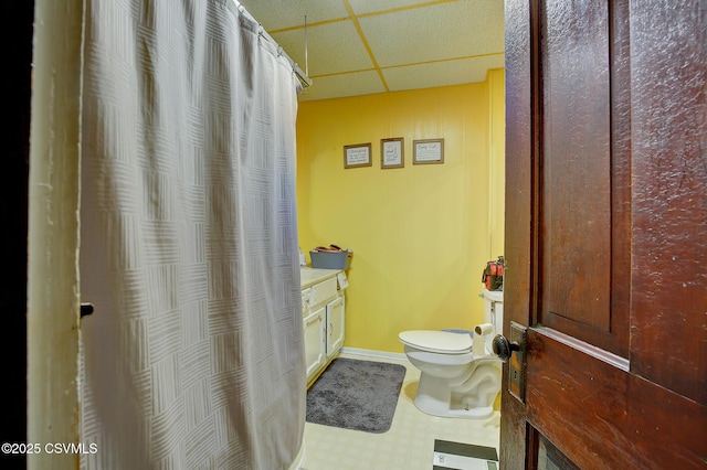 full bathroom featuring toilet, a drop ceiling, a shower with shower curtain, baseboards, and vanity