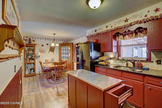 kitchen with a sink, decorative light fixtures, light wood-type flooring, backsplash, and black refrigerator with ice dispenser