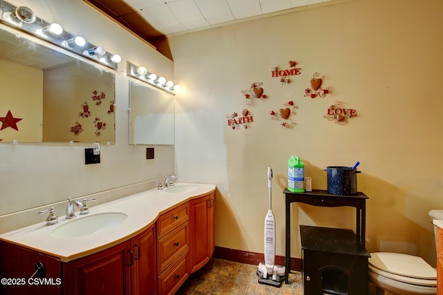 bathroom with double vanity, toilet, baseboards, and a sink