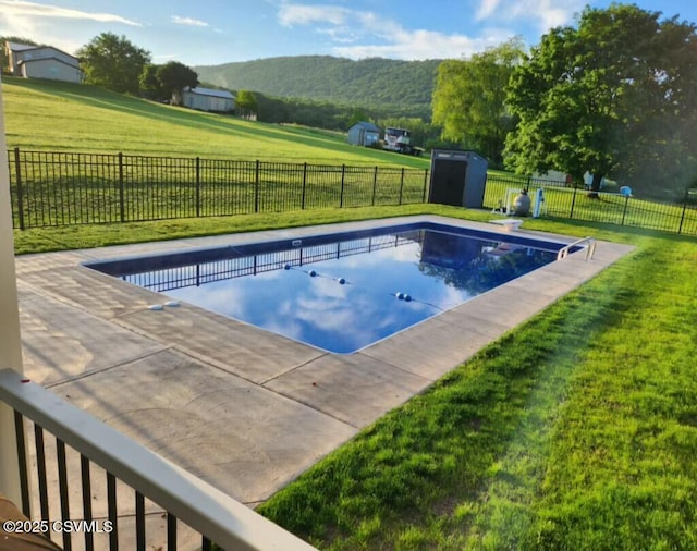 view of swimming pool featuring an outbuilding, a storage unit, a lawn, and a fenced backyard