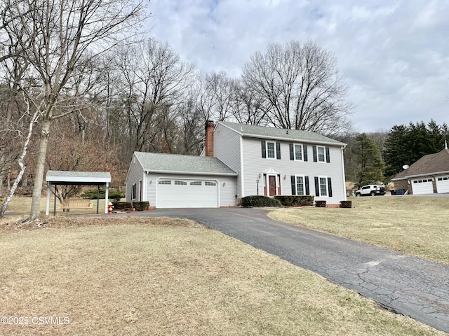 colonial-style house featuring aphalt driveway, a garage, a chimney, and a front lawn