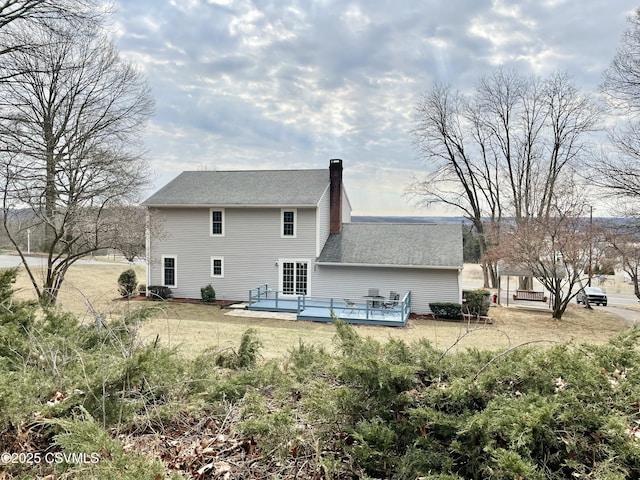 back of house featuring a wooden deck, a lawn, a chimney, and a shingled roof