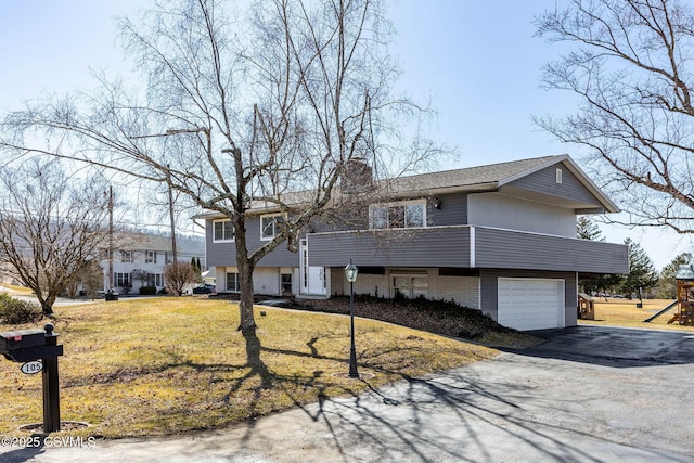 raised ranch with driveway, a playground, a front yard, a garage, and a chimney