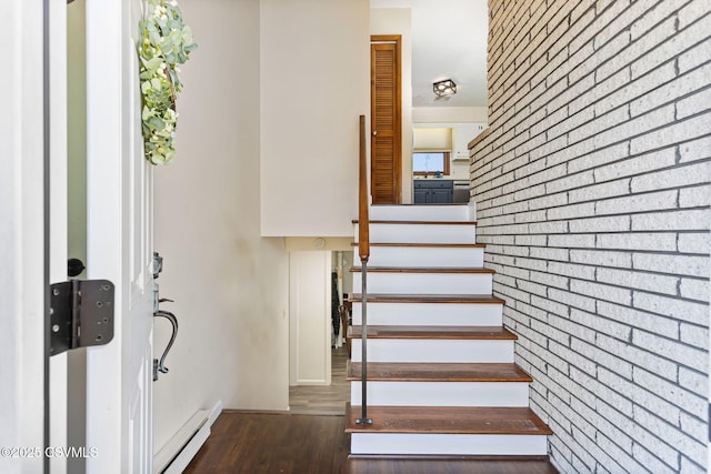 stairs with wood finished floors, brick wall, and a baseboard radiator