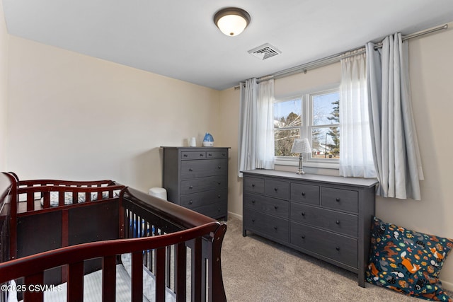 bedroom with visible vents, a crib, and light colored carpet