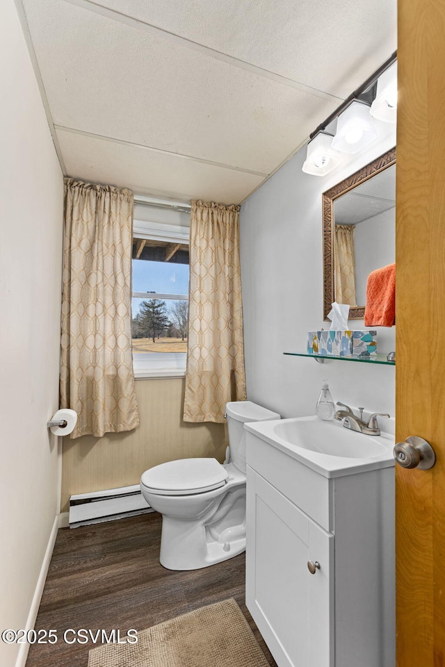 bathroom featuring toilet, wood finished floors, baseboards, baseboard heating, and vanity