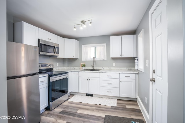 kitchen with light stone counters, appliances with stainless steel finishes, white cabinetry, and a sink