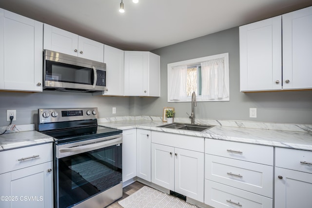 kitchen with light stone counters, light wood-style flooring, a sink, appliances with stainless steel finishes, and white cabinetry