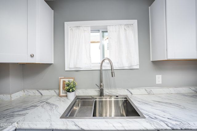 kitchen featuring white cabinets, light stone counters, and a sink