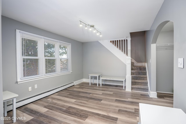 living area featuring wood finished floors, baseboards, a baseboard radiator, arched walkways, and stairs