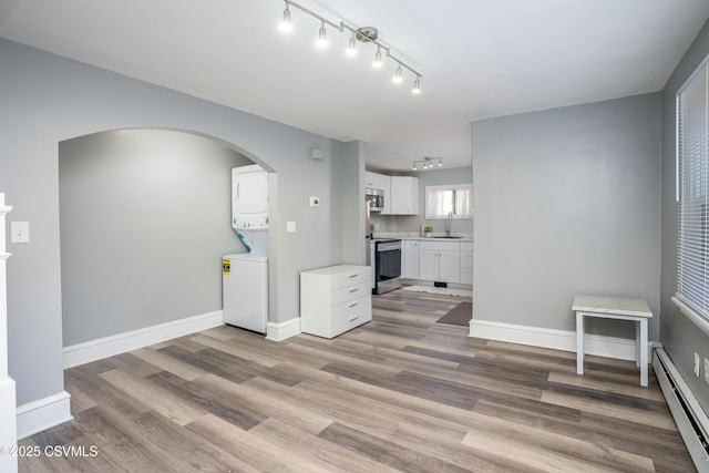 living area featuring a baseboard heating unit, stacked washer / dryer, wood finished floors, and baseboards