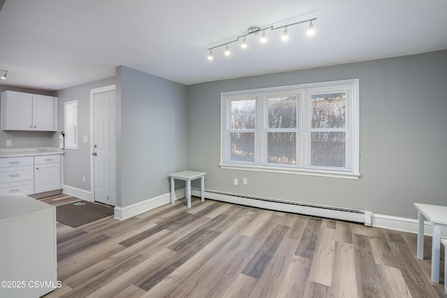 unfurnished dining area with a baseboard heating unit, baseboards, track lighting, and light wood finished floors