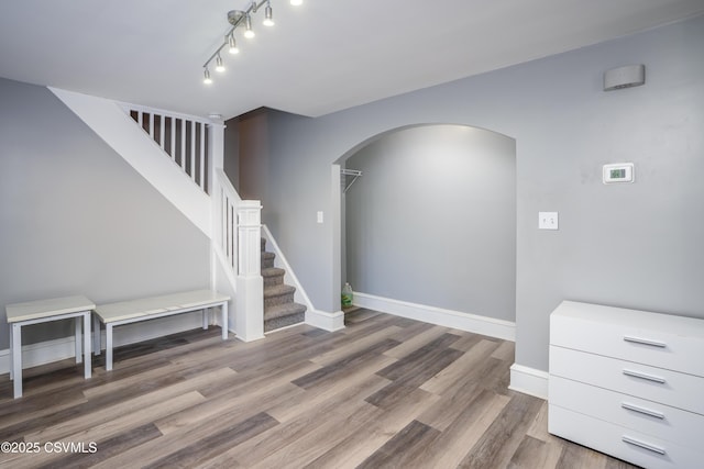 staircase with baseboards, arched walkways, wood finished floors, and track lighting