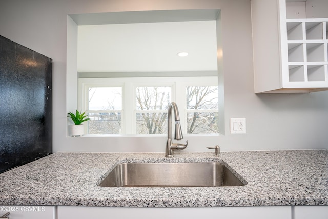 kitchen with a sink, plenty of natural light, light stone counters, and white cabinets