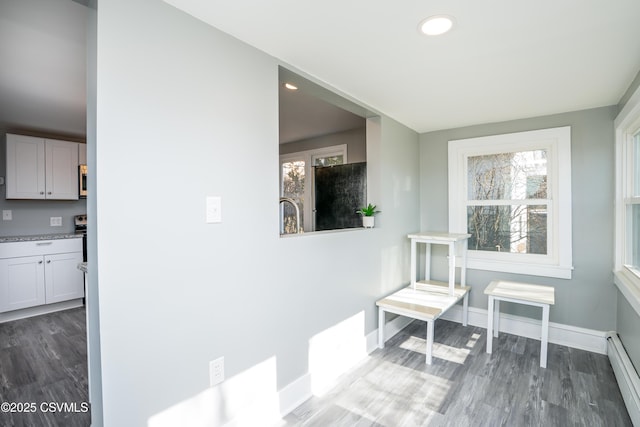 corridor with baseboard heating, recessed lighting, baseboards, and wood finished floors